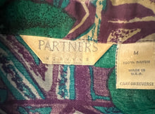 Load image into Gallery viewer, A medium vintage Partners Mervyns short sleeve button up with a purple and blue all-over floral print. The shirt is missing all of the buttons but one and has been well-worn. Measured FlatChest - 36&quot;Sleeve - 9&quot;Length - 28&quot;