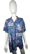 Load image into Gallery viewer, A medium vintage Partners Mervyns short sleeve button up with a purple and blue all-over floral print. The shirt is missing all of the buttons but one and has been well-worn. Measured FlatChest - 36&quot;Sleeve - 9&quot;Length - 28&quot;